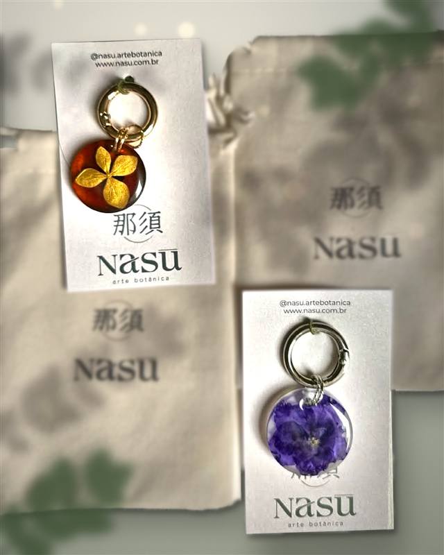 Os dois prêmios: um chaveiro de resina âmbar com uma flor dourada e um chaveiro transparente com uma flor roxa, nos cartões da NASU arte botânica